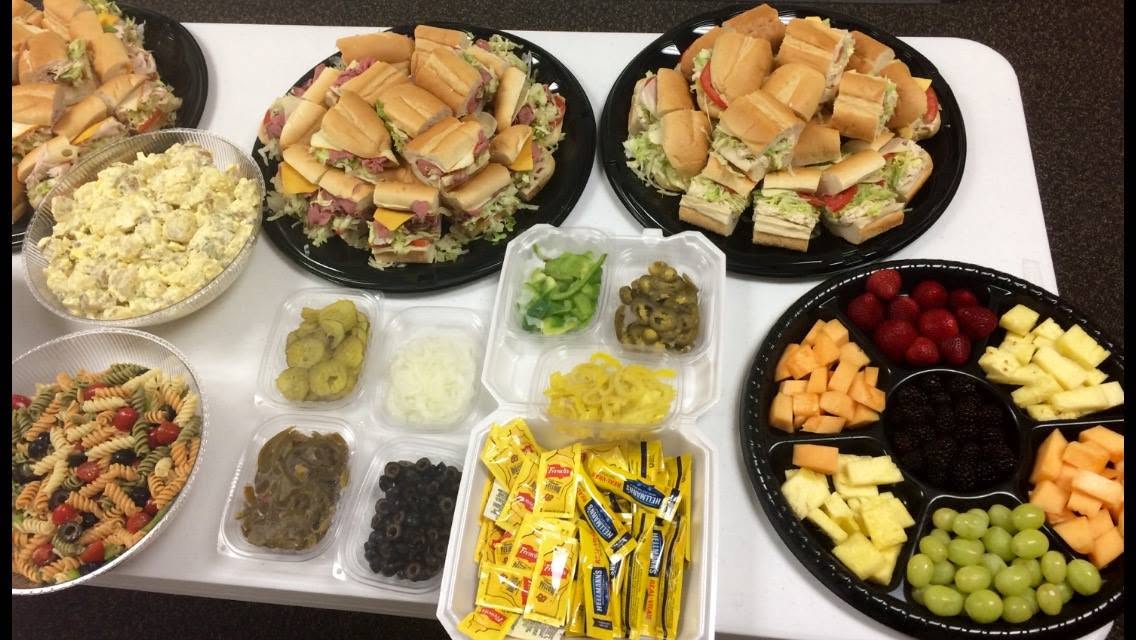 A catering spread of subs, salads, fruit and condiments