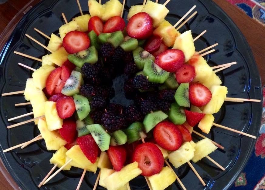 A circular platter of colorful fruit skewers